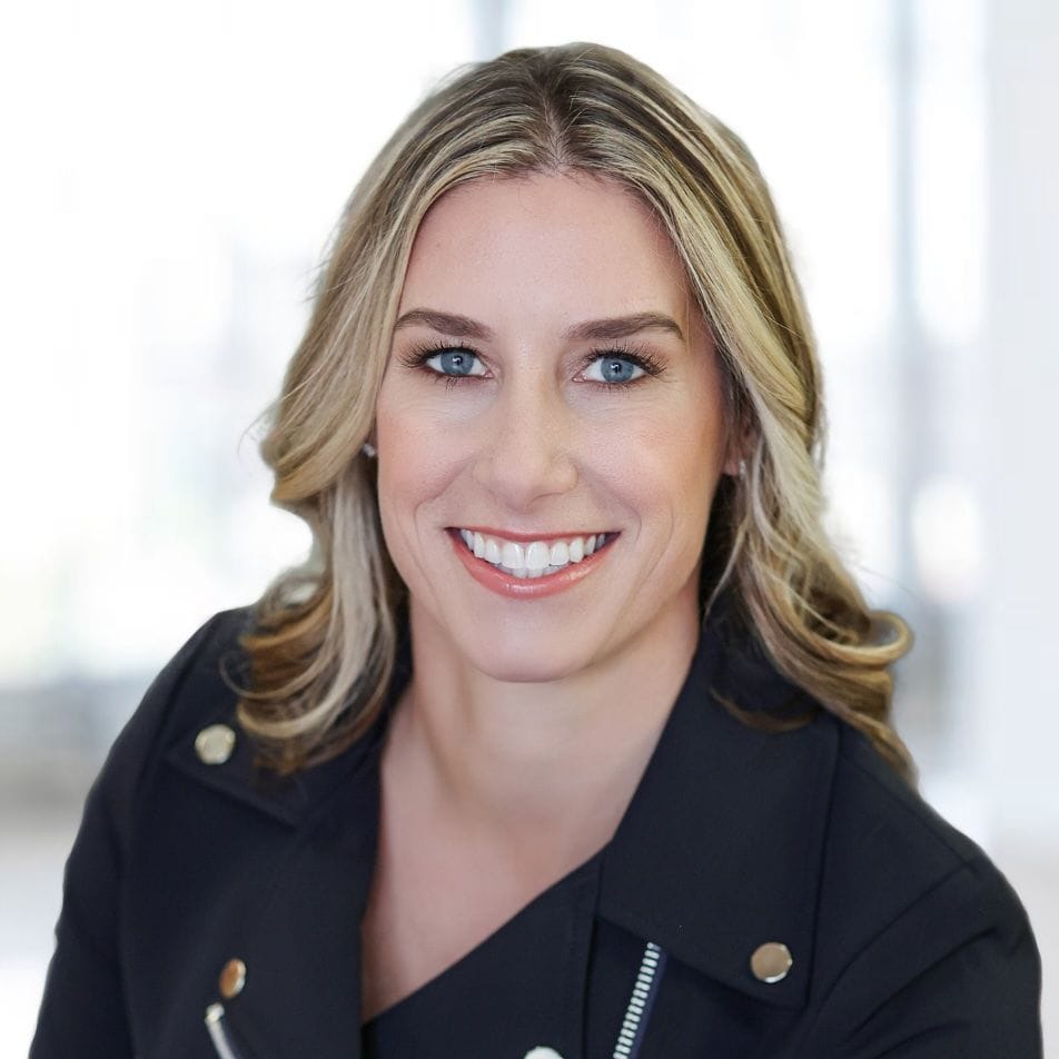 Smiling blonde woman in a black jacket, posing for a professional headshot.