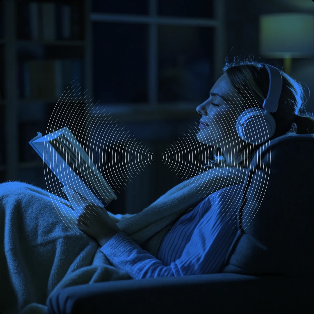A woman wearing headphones, reading a book in a dark room with a blue glow.