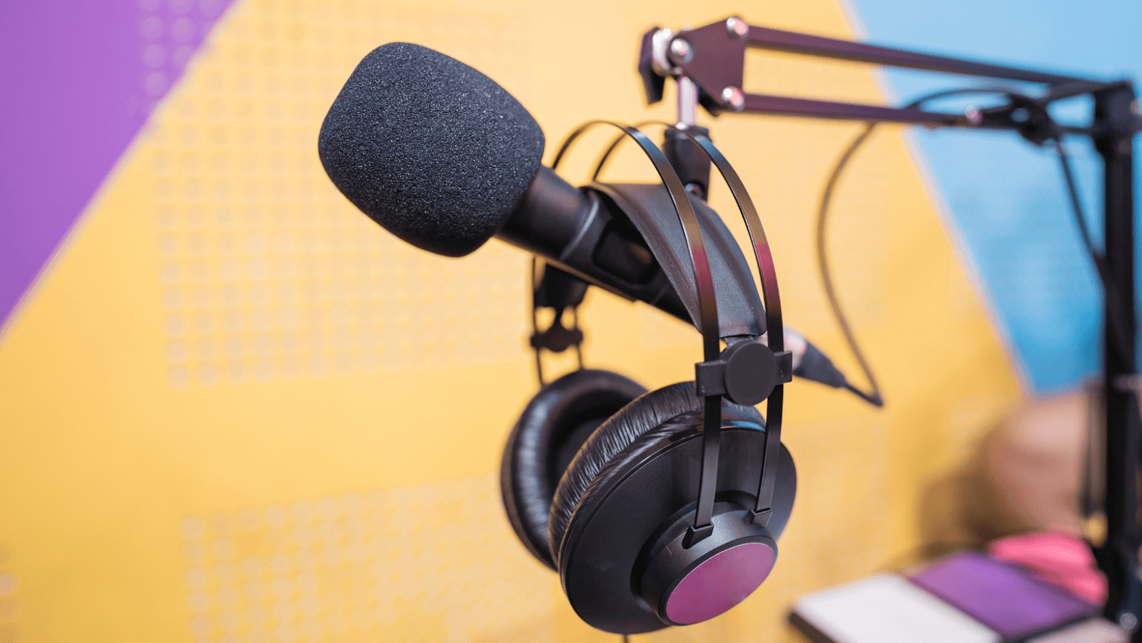 A microphone and headphones hanging on a stand against a colorful background.