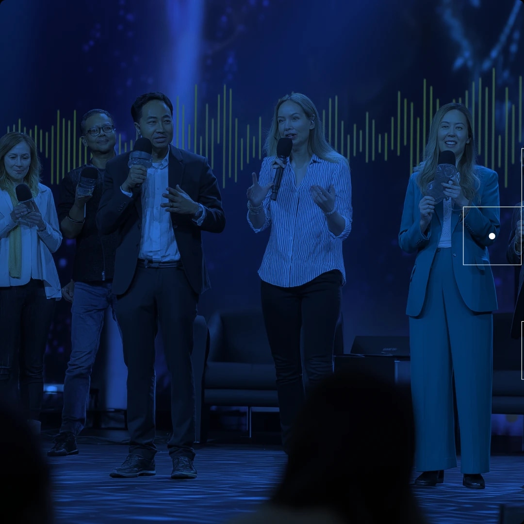 Group of people speaking on stage with microphones, in front of a digital sound wave background.