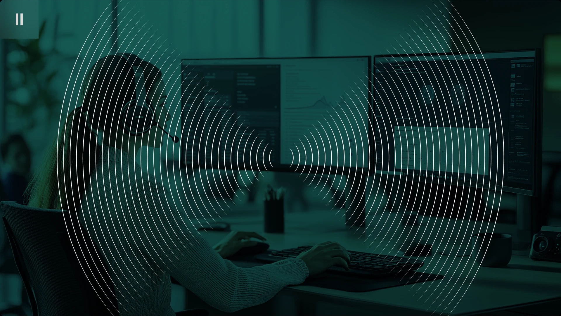 Person working at a computer with dual monitors, wearing a headset.