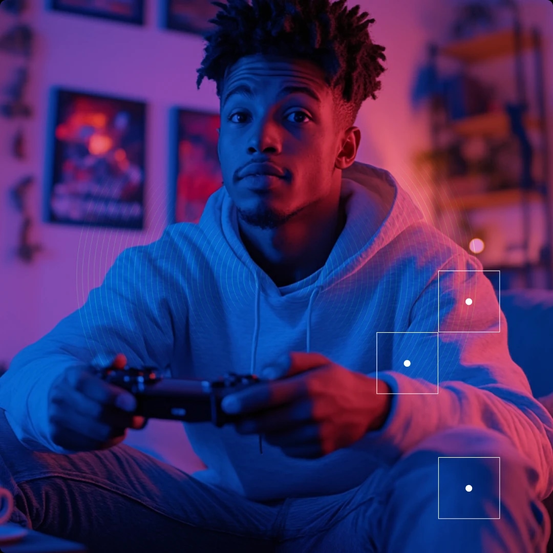 A young man sitting on the floor, holding a game controller, illuminated by colorful neon lighting.