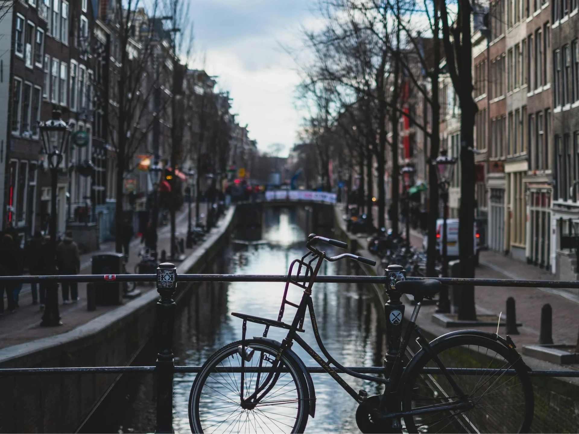 A bicycle parked on a bridge over a canal in a city street with buildings and trees lining the waterway.